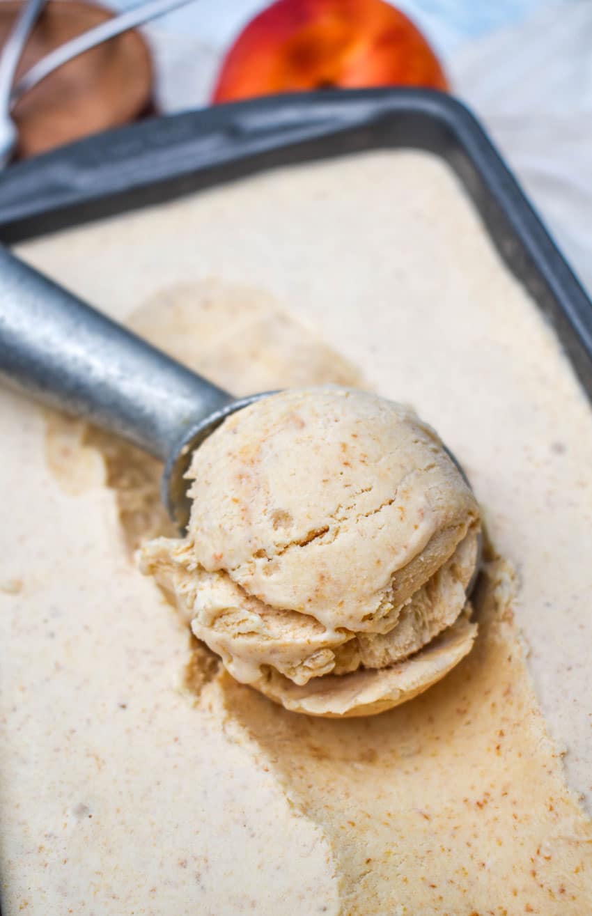a metal scoop scooping no churn peach ice cream out of a metal loaf pan