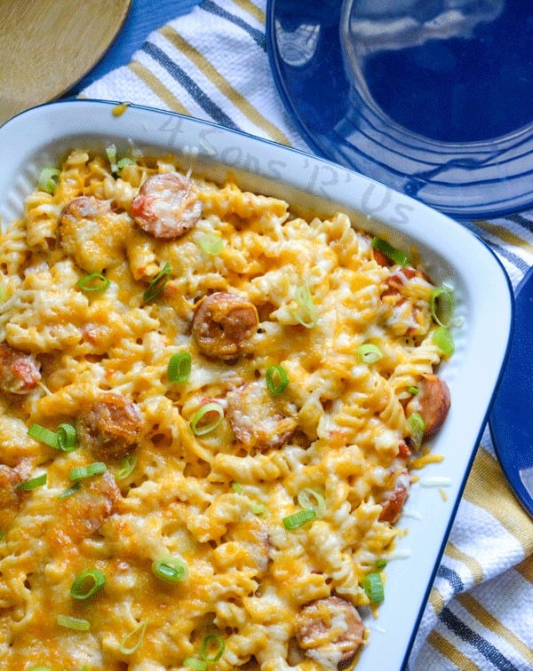 Spicy Sausage and Pasta Casserole in a white casserole dish, shown on top of a striped dishcloth with a wooden spoon and blue serving plates in the background