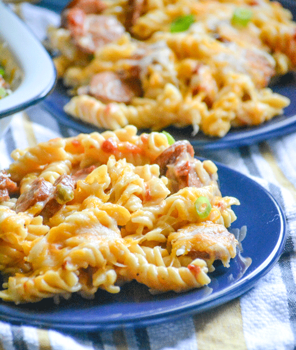 Spicy Sausage and Pasta Casserole is shown on a navy blue plate on a striped dish towel with another plate of the pasta dish in the background