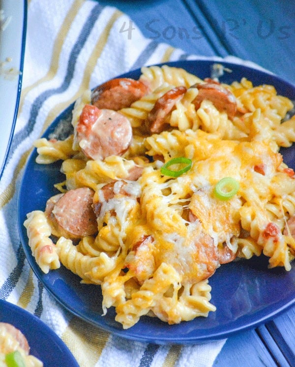 cheesy sausage and pasta casserole served on a blue plate set on top of a striped dish towel on top of a wooden blue back ground