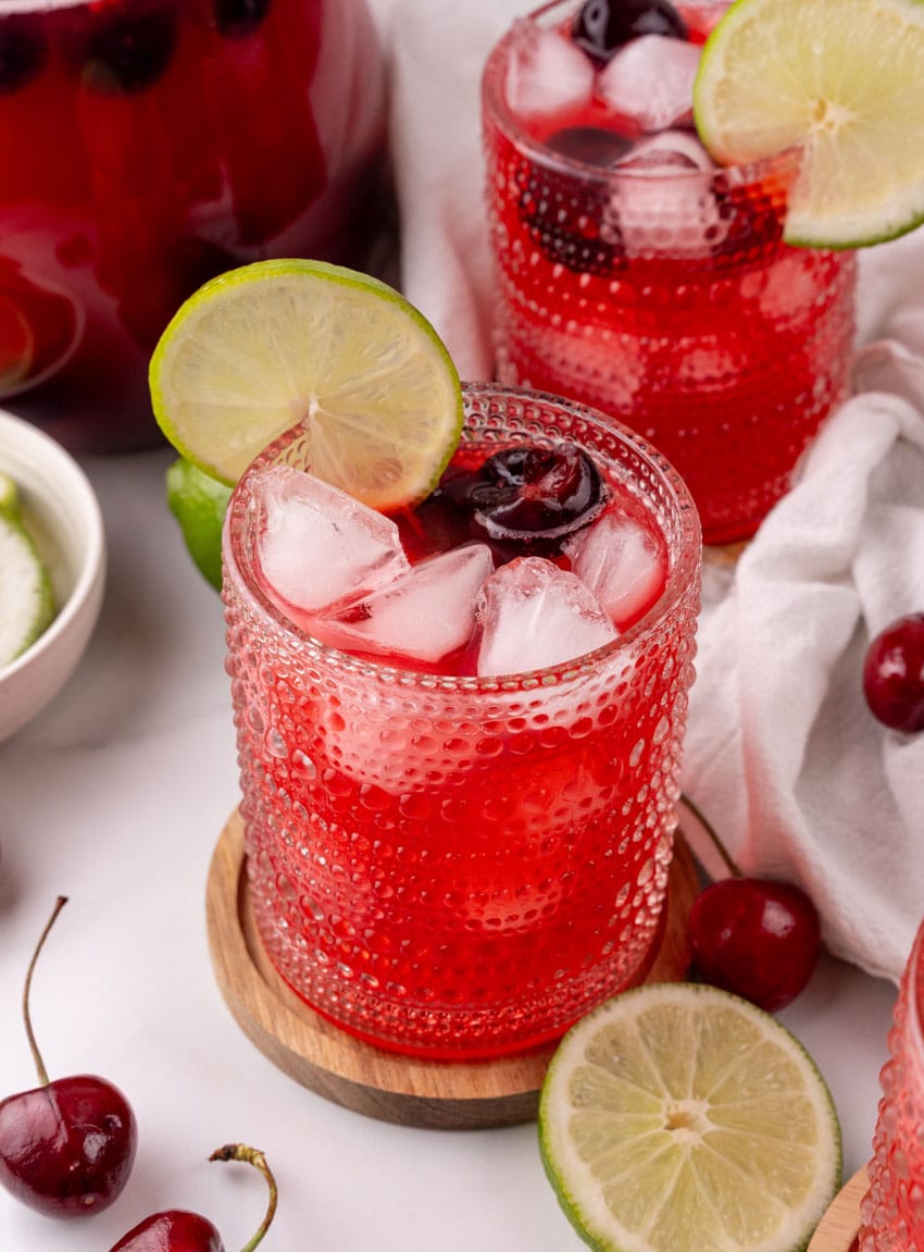 sweet black cherry limeade with ice in a small glass on a wooden coaster