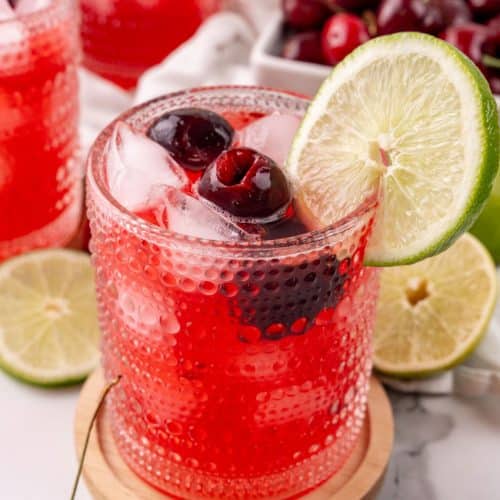 sweet black cherry limeade with ice in a small glass on a wooden coaster