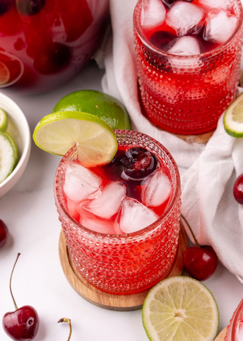 sweet black cherry limeade with ice in a small glass on a wooden coaster
