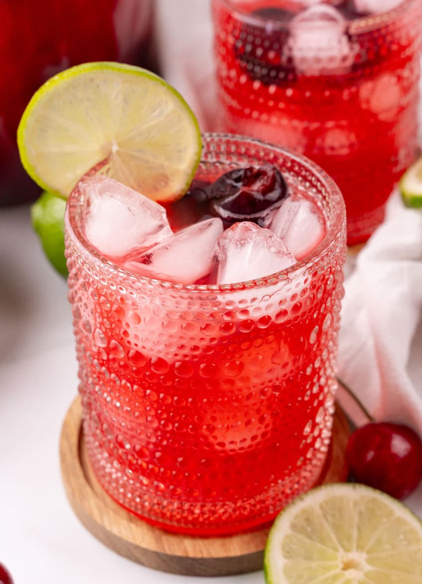 sweet black cherry limeade with ice in a small glass on a wooden coaster
