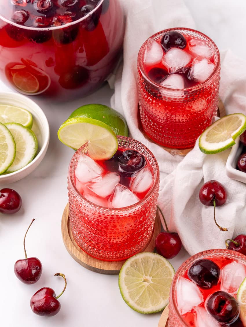 sweet black cherry limeade with ice in a small glass on a wooden coaster