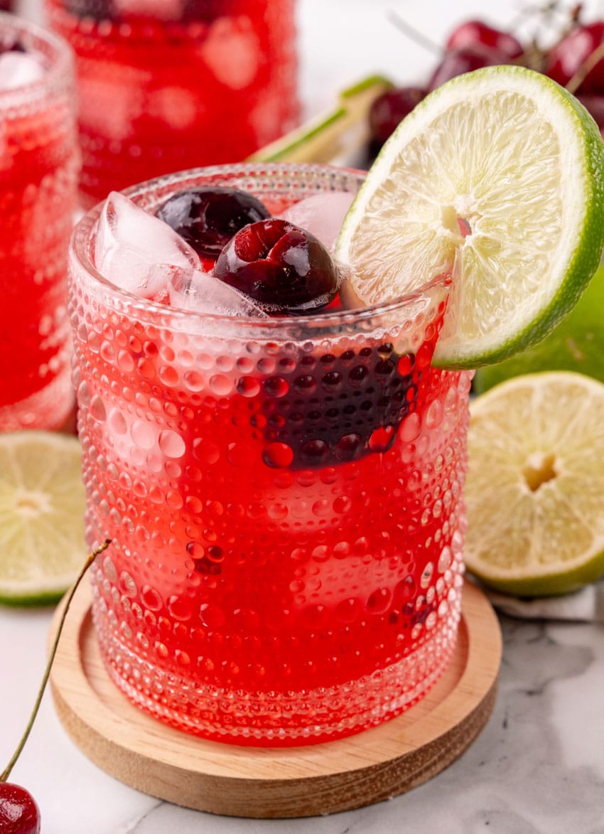 sweet black cherry limeade with ice in a small glass on a wooden coaster