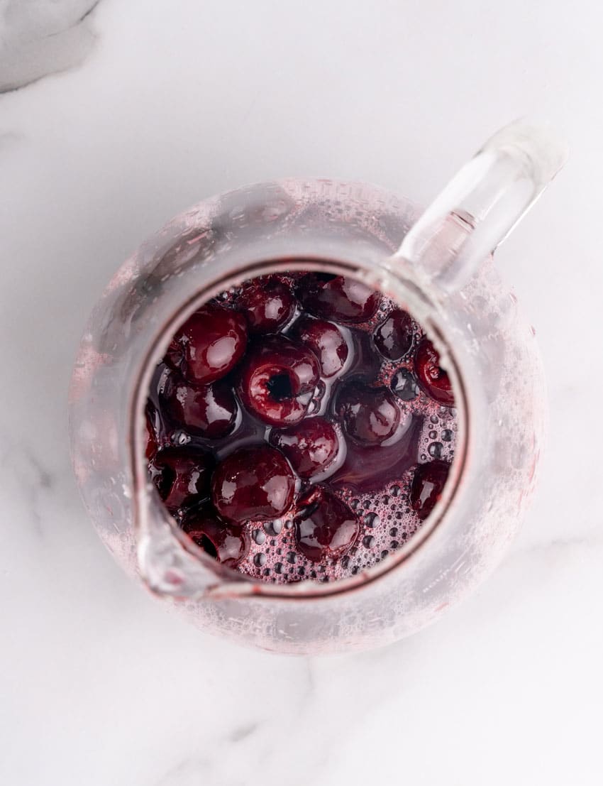 sweet dark cherries in orange juice in a glass pitcher