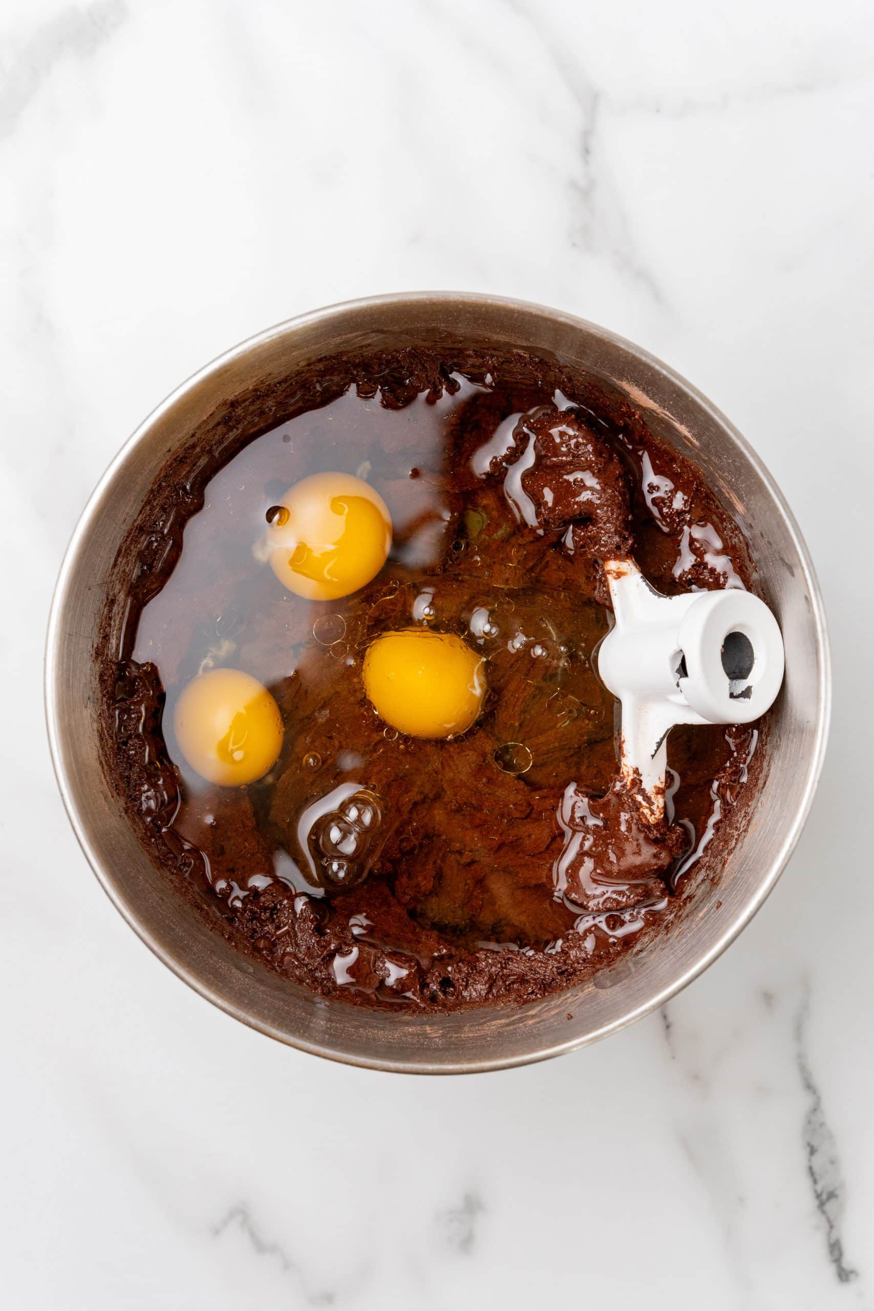 eggs and oil in a metal mixing bowl with chocolate cake batter