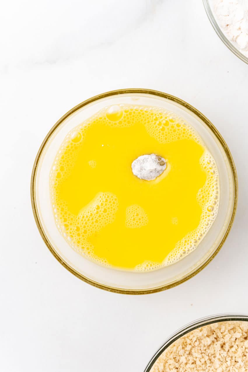 a flour coated olive in egg wash in a small glass bowl