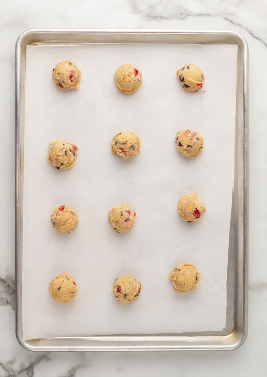 balls of strawberry chocolate chip cookie dough arranged in rows on a parchment paper lined baking sheet