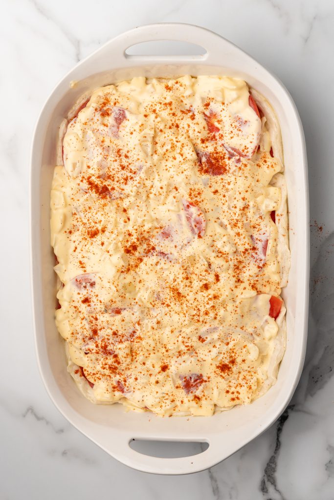 mayo and cheese sauce spread out over sliced tomatoes in a white casserole dish