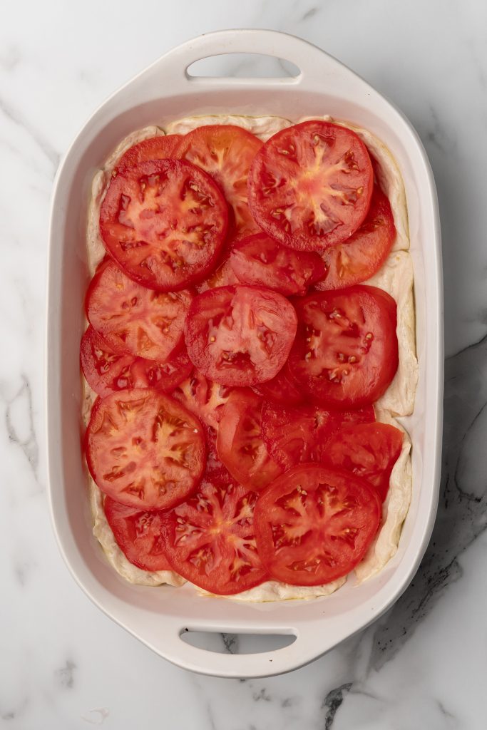 tomato slices layered on a biscuit crust in a white casserole dish