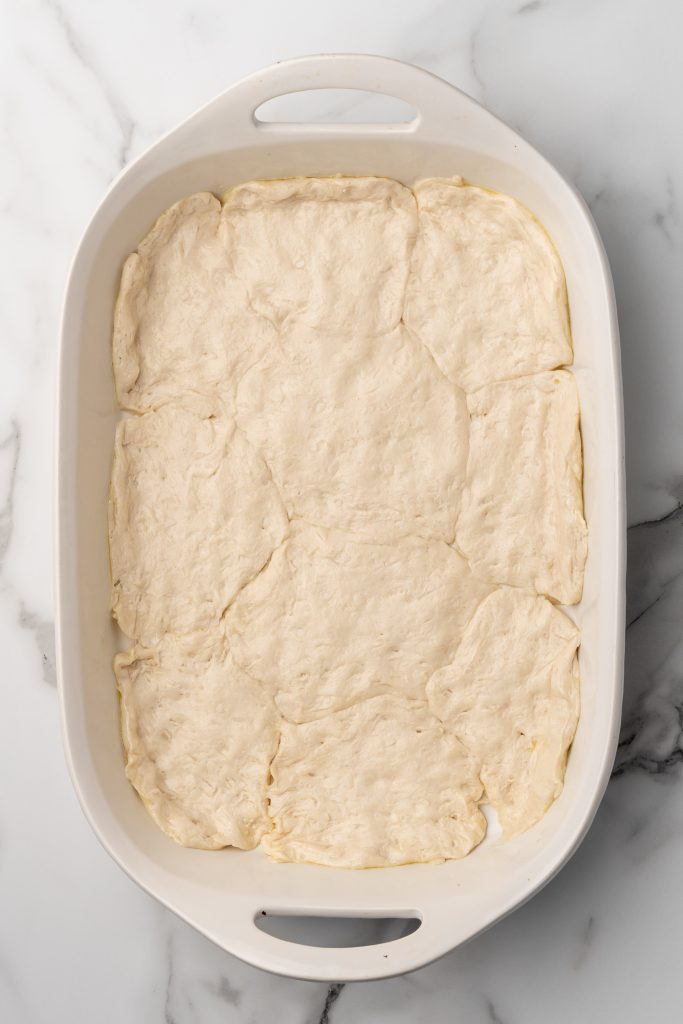 canned biscuits smashed together in the bottom of a white casserole dish to form a crust