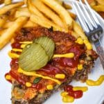 a slice of cheeseburger pie topped with ketchup and mustard next to crispy french fries on a white plate