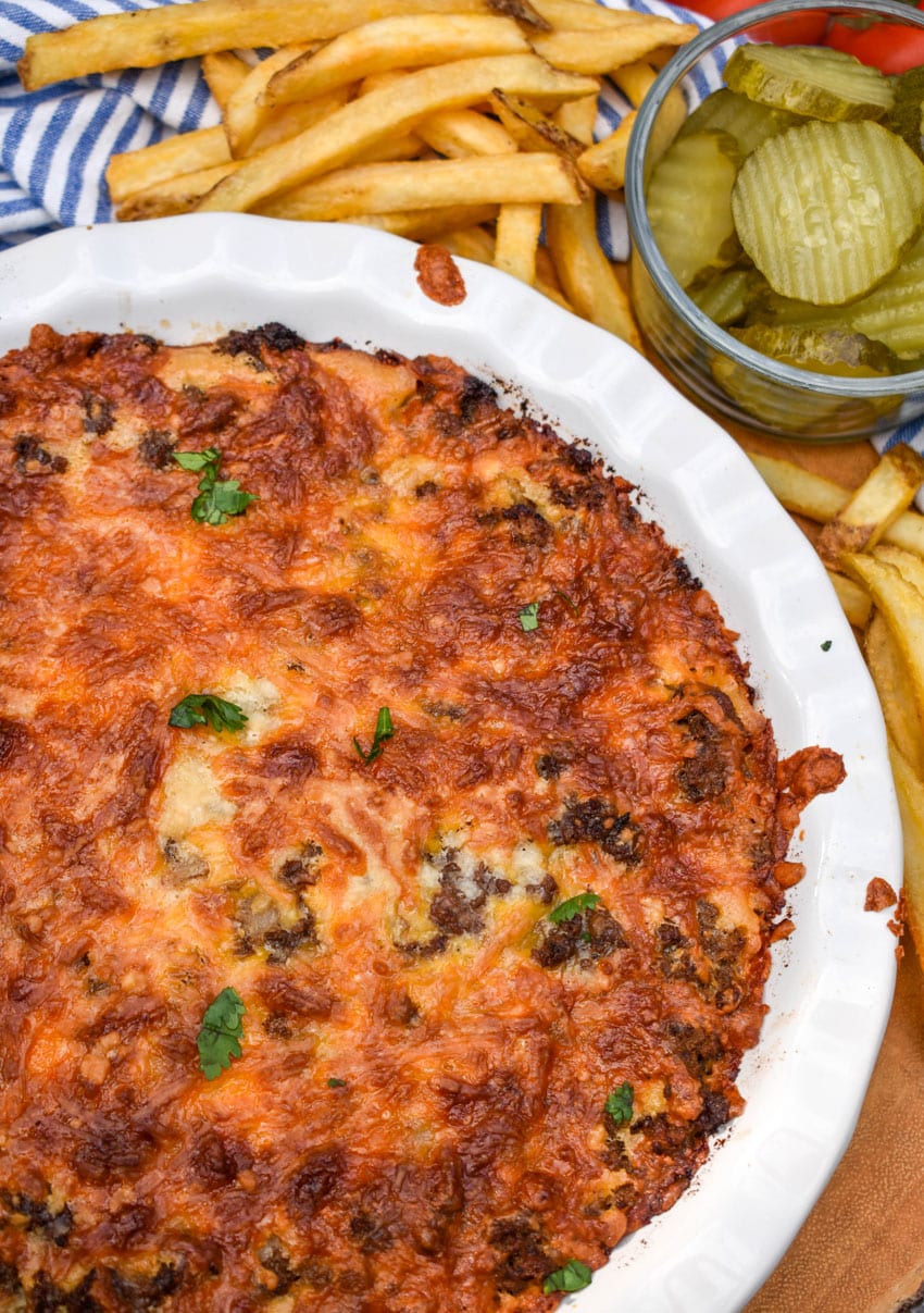 a homemade bisquick cheeseburger pie in a white pie plate with crispy french fries in the background