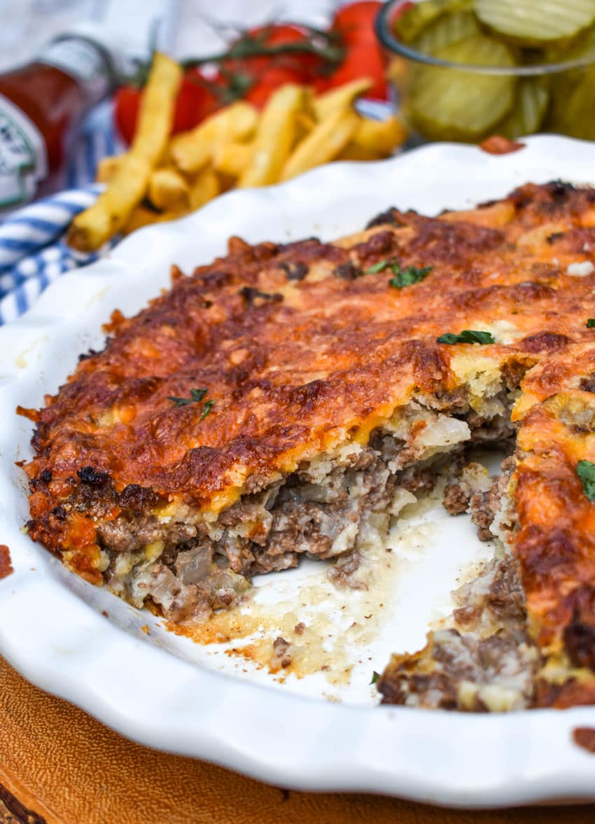 impossible cheeseburger pie in a white pie dish with a slice remove to show the filling