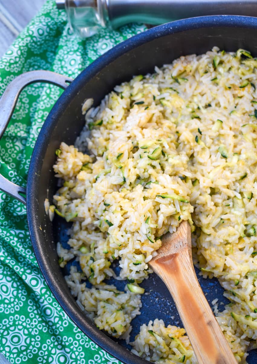a wooden spoon stuck in a skillet of cheesy zucchini rice