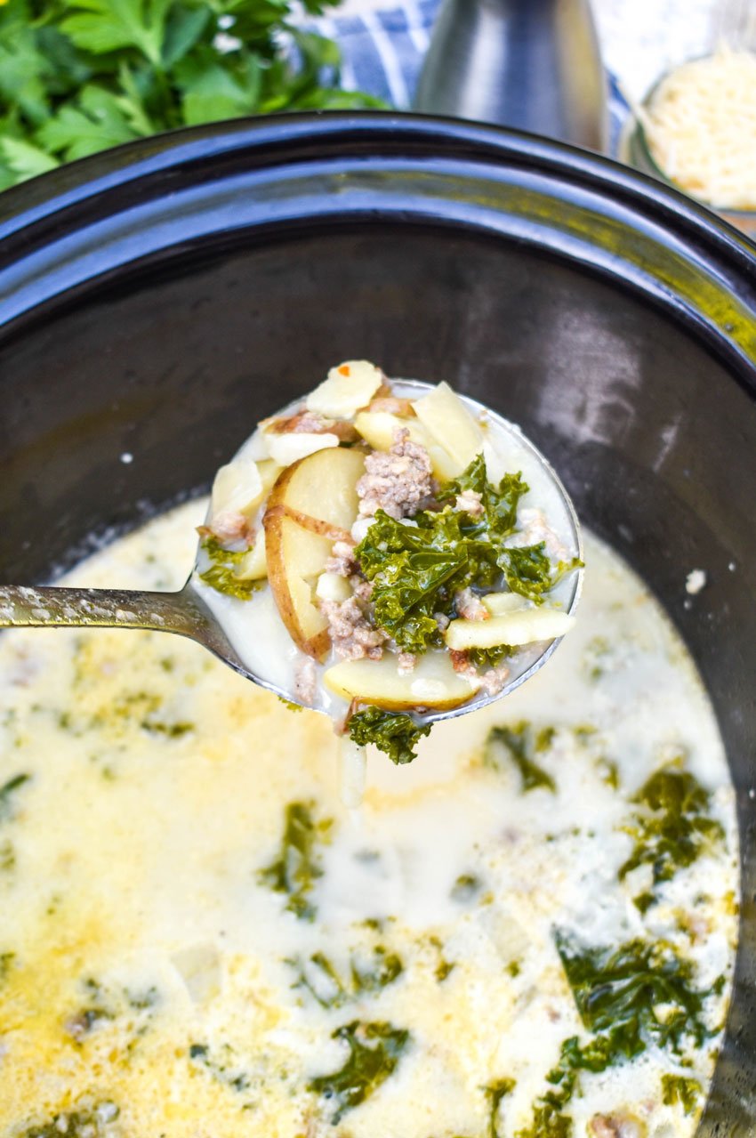 a silver ladle holding a scoop of zuppa toscana above a black crockpot