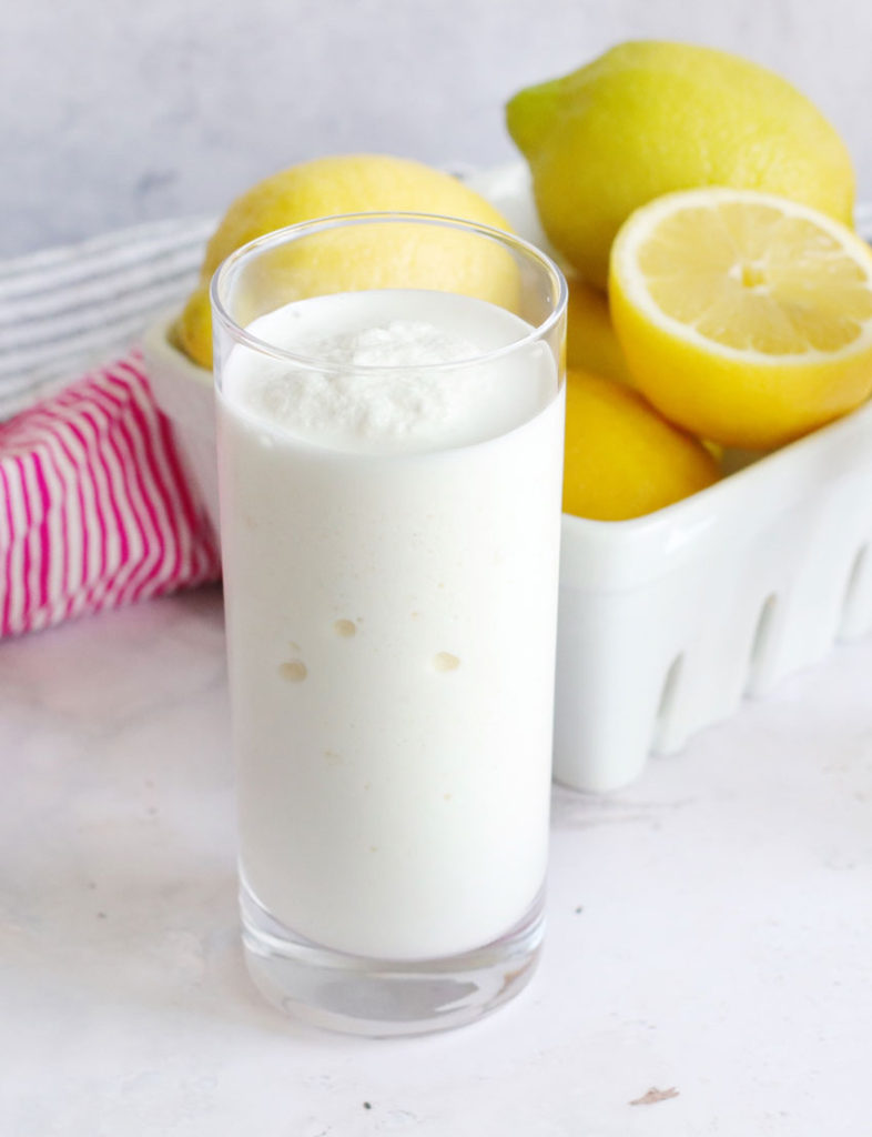 copy cat chick fil a frosted lemonade shown in a clear glass set in front of a white basket filled with yellow lemons