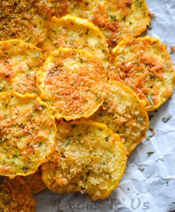 crispy yellow squash chips piled on white parchment paper sprinkled with dried herbs