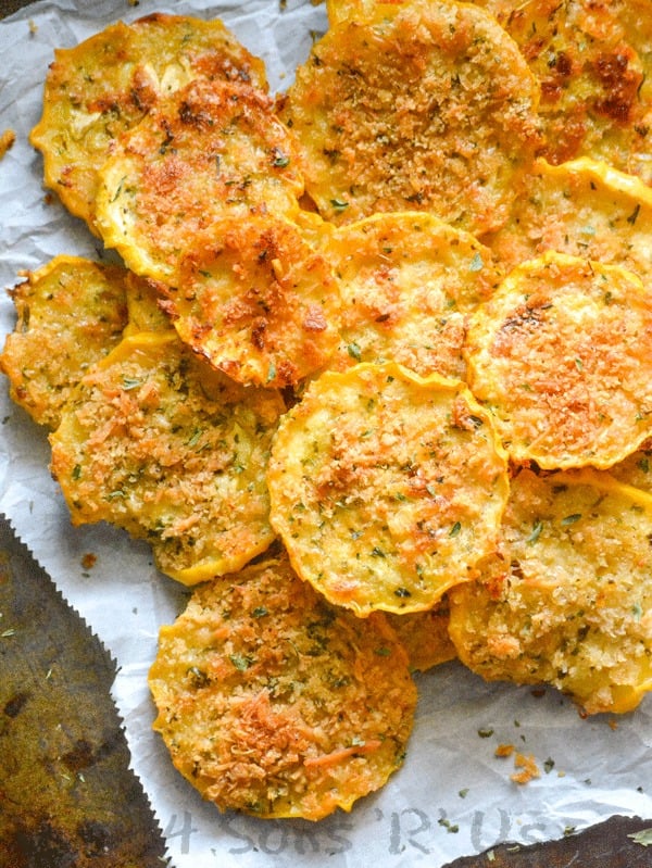 Crispy Garlic Parmesan Squash Chips piled on a piece of white parchment paper sprinkled with dried herbs