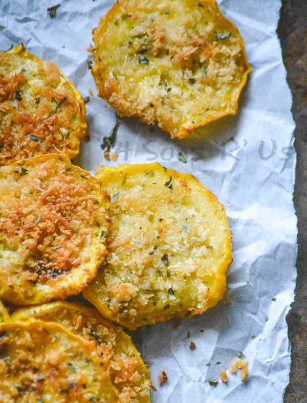 Crispy Garlic Parmesan Squash Chips shown on white parchment paper with chopped herbs