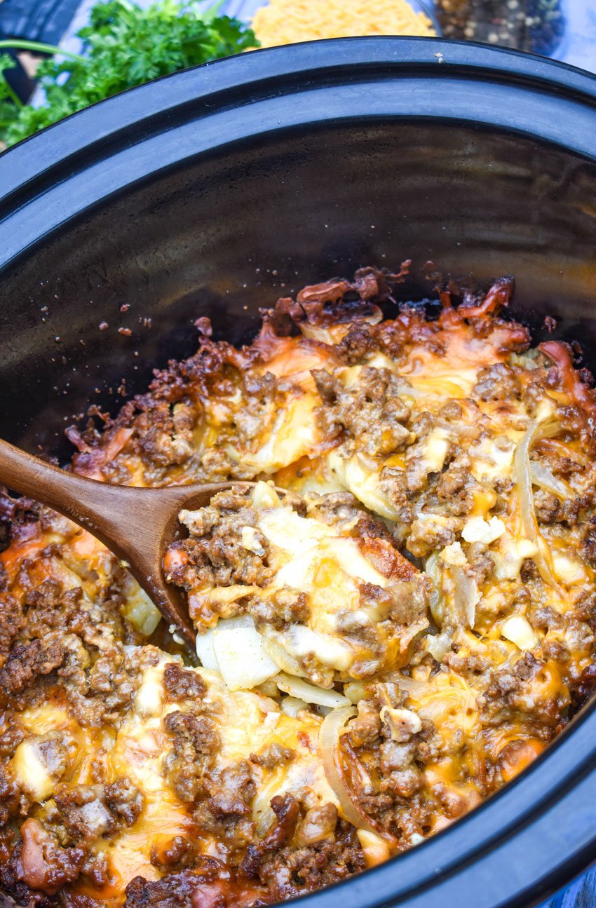 a wooden spoon in a crockpot filled with cheesy ground beef and potatoes