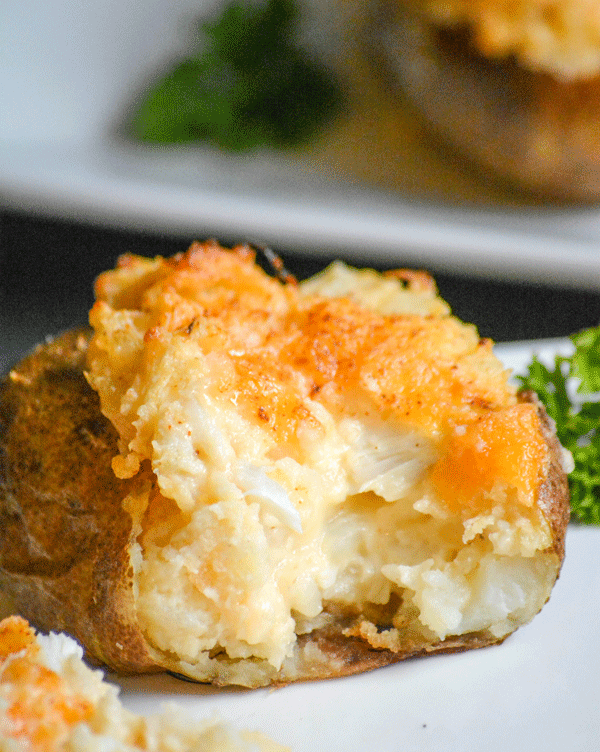 a twice baked crab stuffed potato on a white plate, opened to reveal the filling