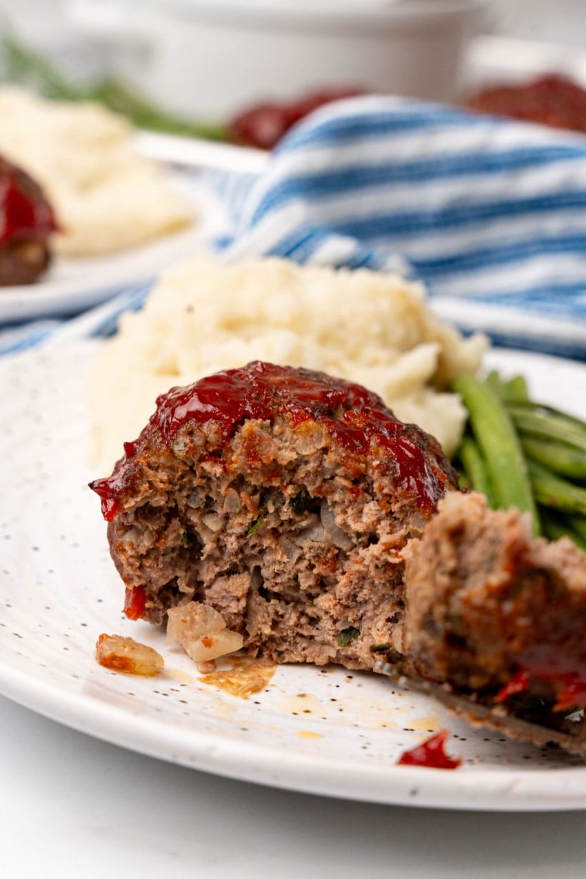 a piece of meatloaf on a small white plate with mashed potatoes and green beans on the side