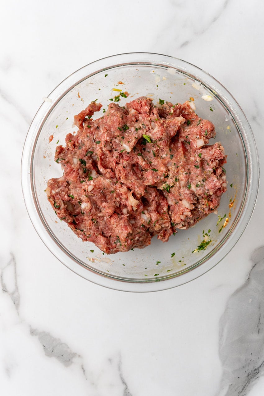 seasoned ground beef mixture for meatloaf in a glass mixing bowl