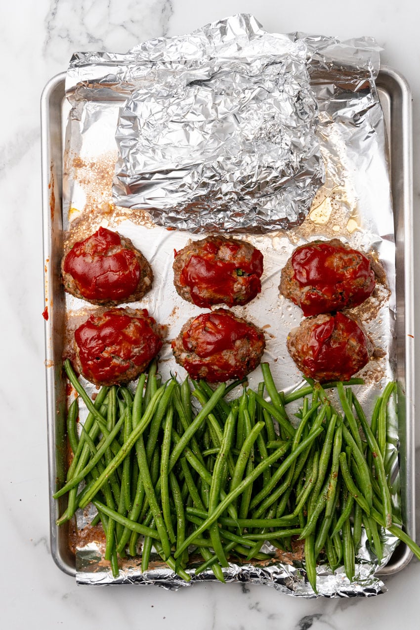 roasted green beans, mini meatloaves, and a bowl of mashed potatoes on a metal sheet pan