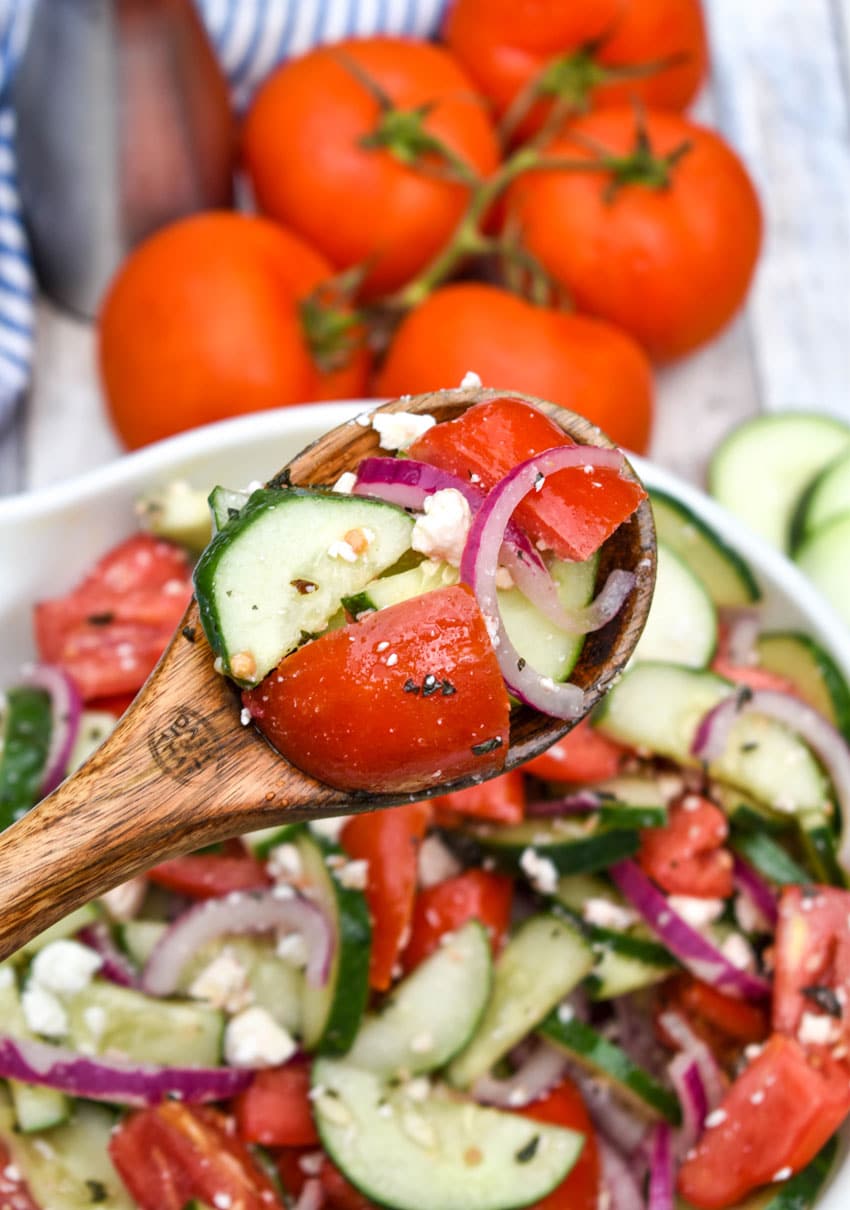a wooden spoon holding up a scoop of tomato salad with cucumbers