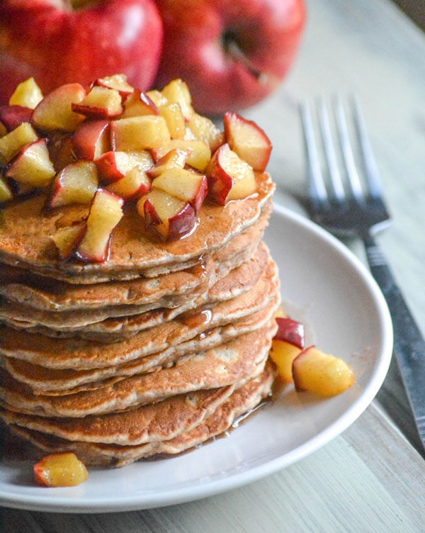 a stack of apple pie pancakes on a white plate next to a silver fork