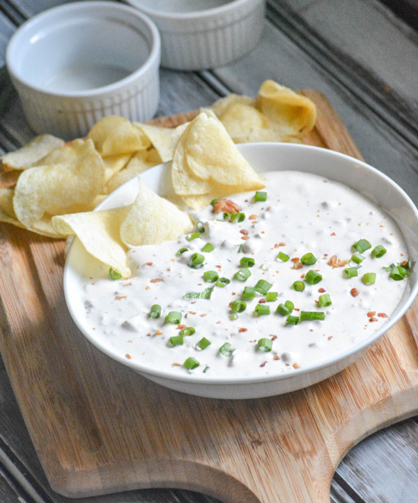 Creamy Bacon Horseradish Dip shown in a white bowl on a wooden cutting board with crisp potato chips