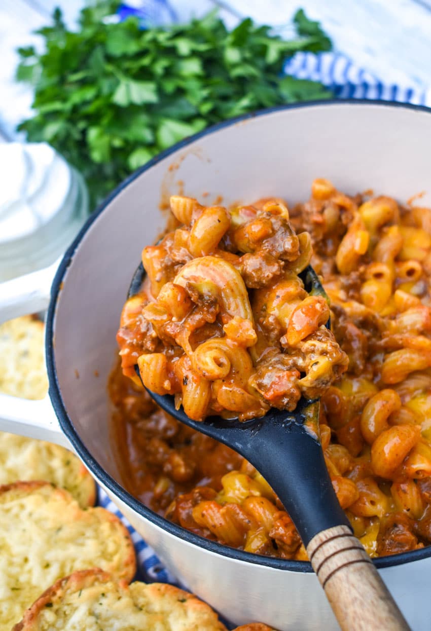 a spoon scooping beefy chili mac out of a white dutch oven
