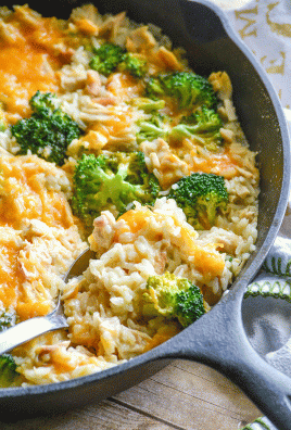 A SILVER SPOON DIGGING INTO A SKILLET OF CHEESY CHICKEN BROCCOLI RICE