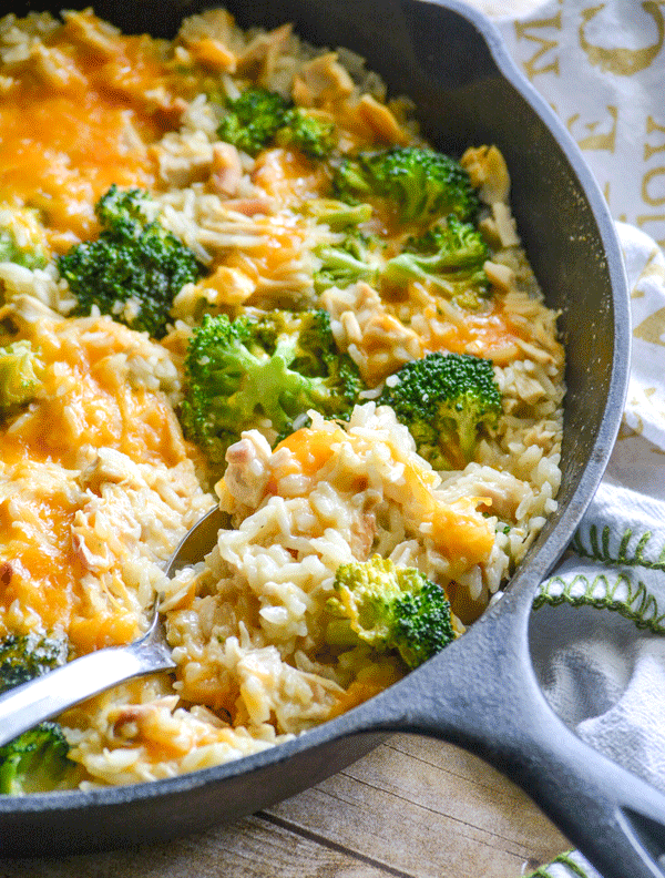 A SILVER SPOON DIGGING INTO A SKILLET OF CHEESY CHICKEN BROCCOLI RICE