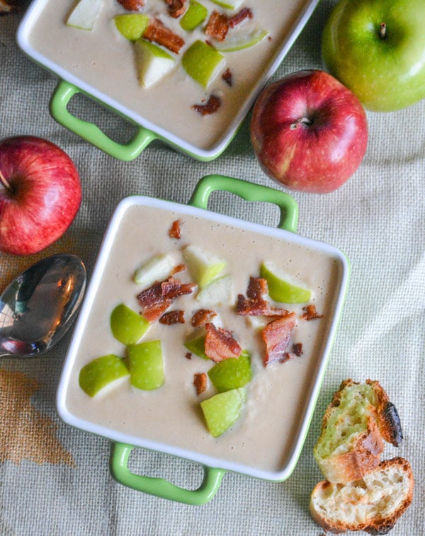 two bowls of roasted apple and white cheddar soup topped with diced apple and crispy pieces of bacon