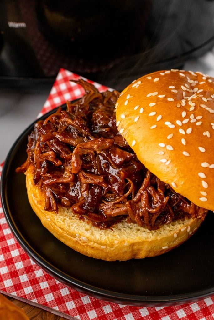 crockpot brisket sandwich on a small black plate resting on a red and white checkered napkin
