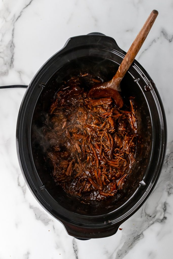 shredded beef brisket tossed with barbecue sauce in the bowl of a crockpot