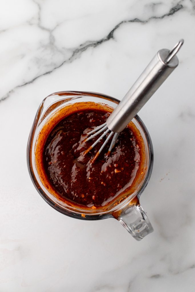 barbecue sauce mixture in a glass measuring cup with a silver whisk