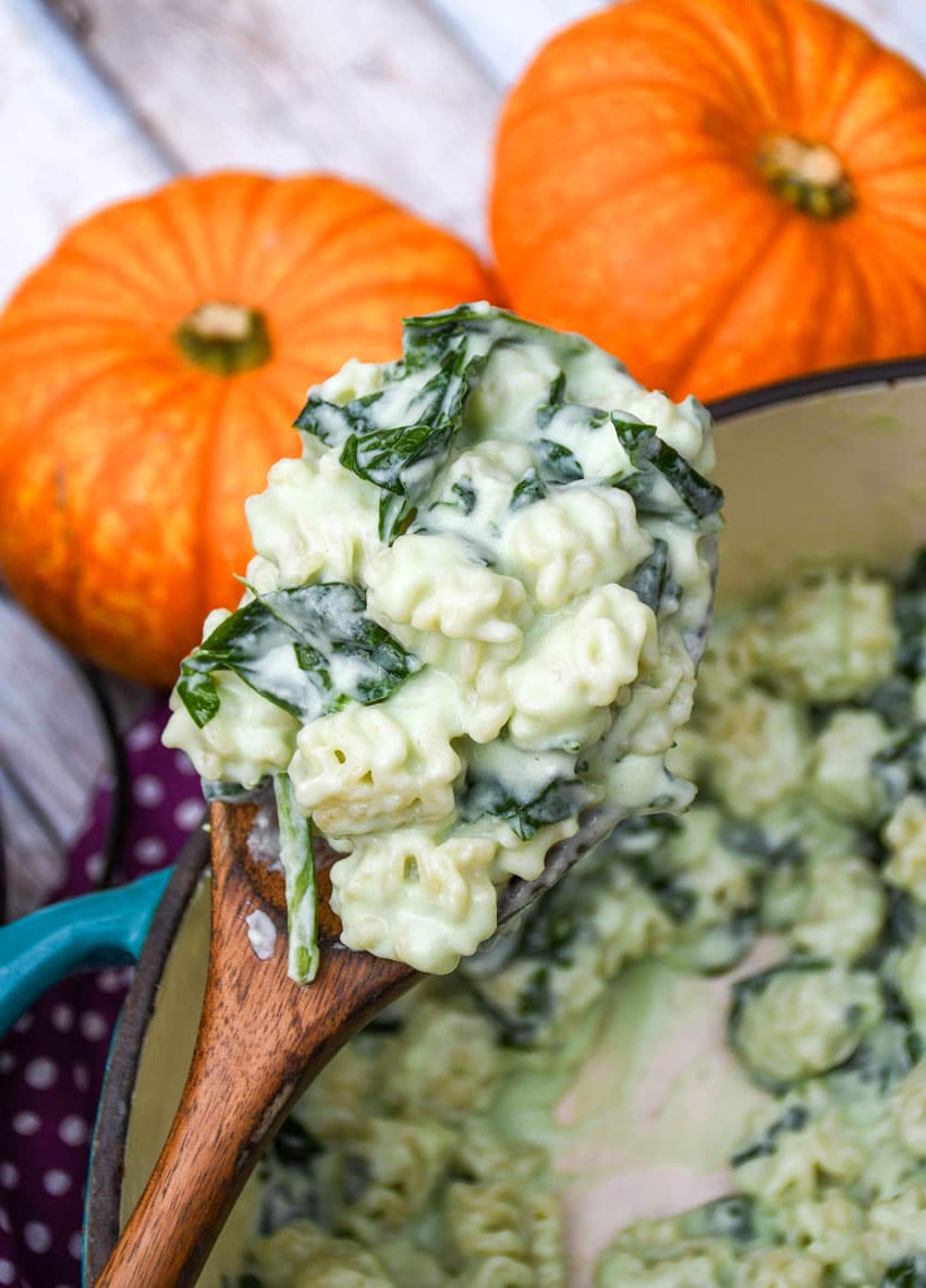 a wooden serving spoon holding up a scoop of white cheddar mac and cheese with spinach
