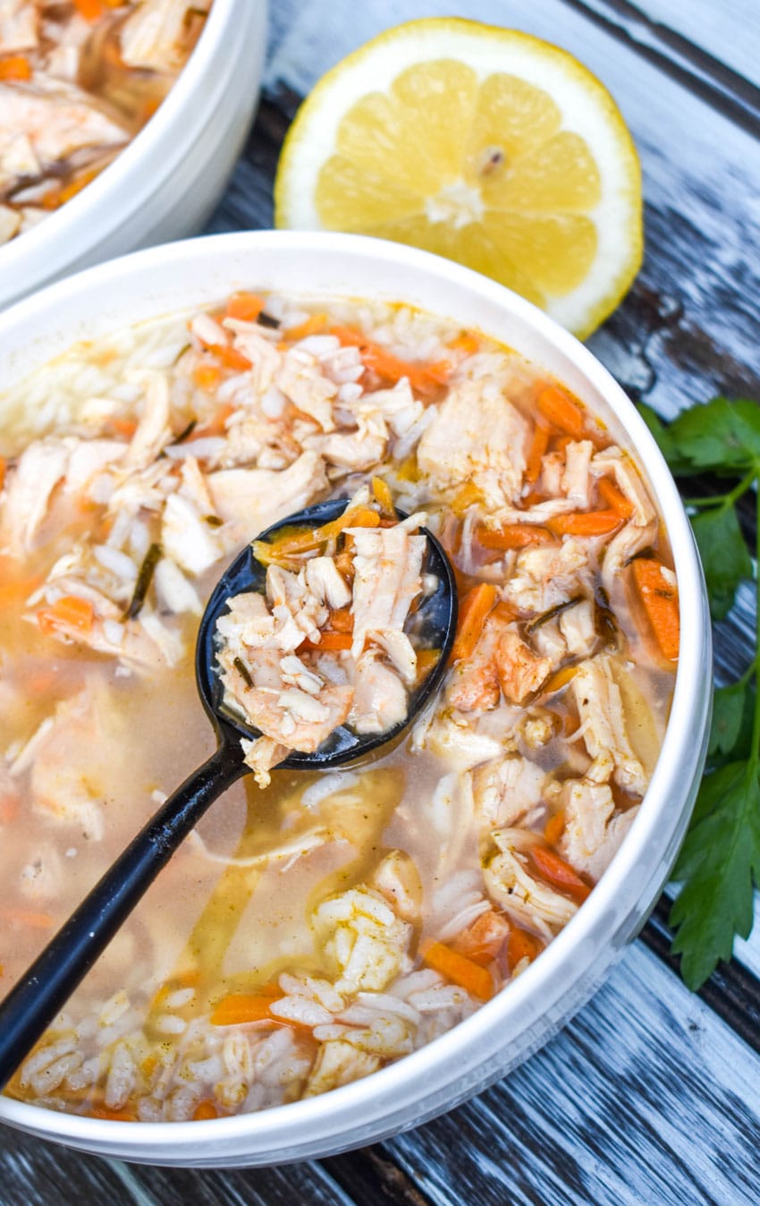 a black spoon scooping taziki's copycat greek lemon chicken soup with rice out of a white bowl