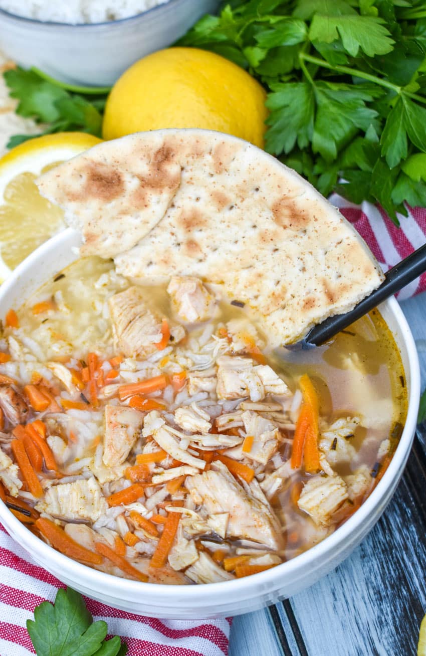 greek lemon chicken soup with rice in a white bowl with a piece of torn pita bread resting against the edge