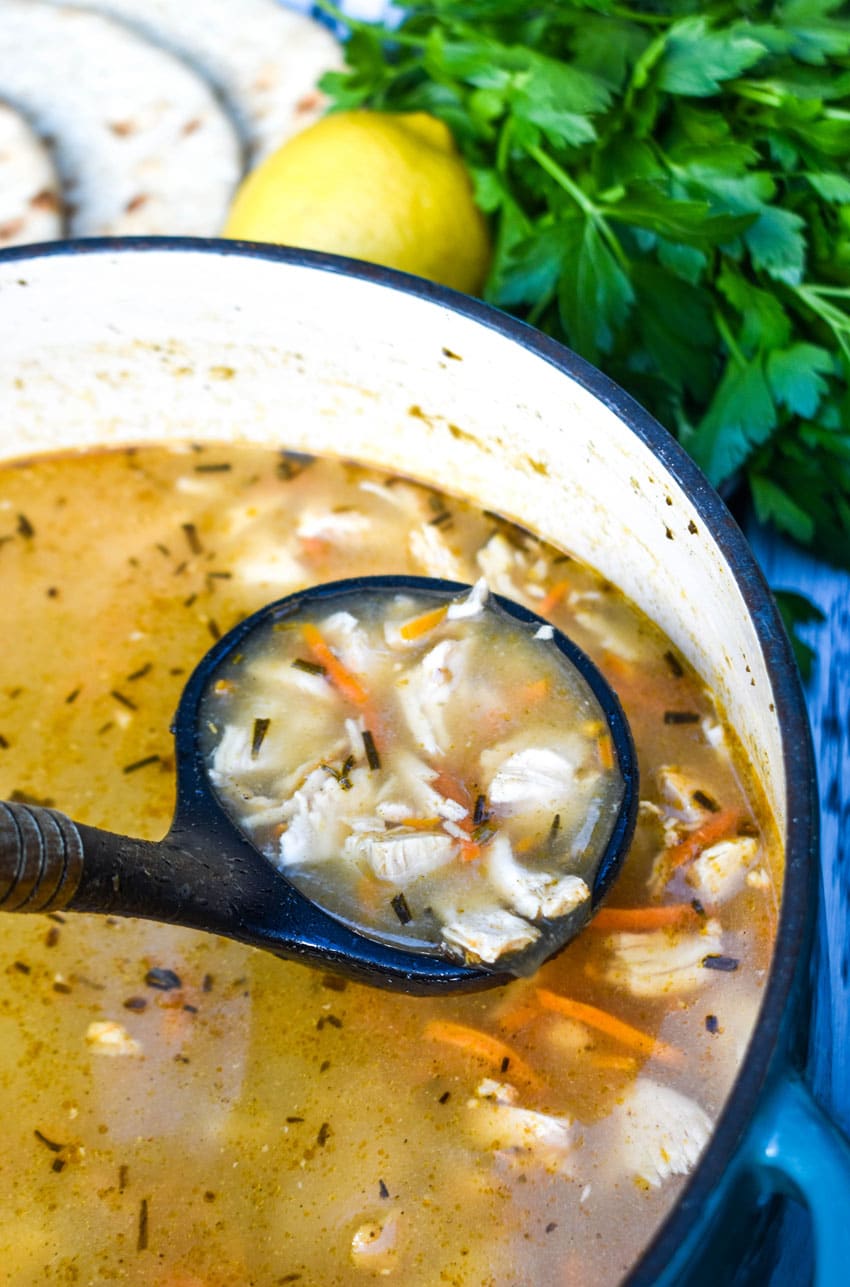 a black ladle scooping greek lemon chicken soup out of a large blue dutch oven