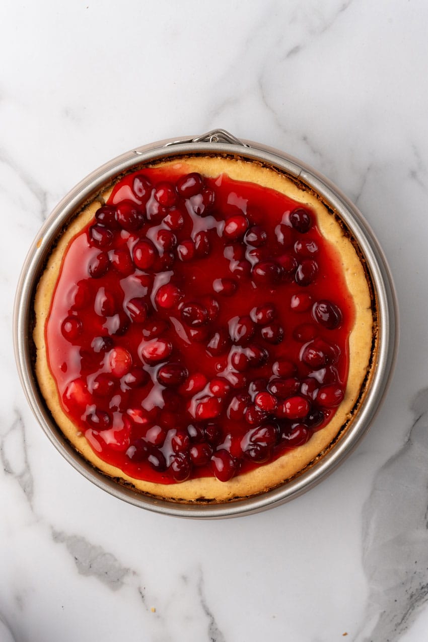 homemade sweetened cranberry sauce spread overtop a baked eggnog cheesecake on a marble counter