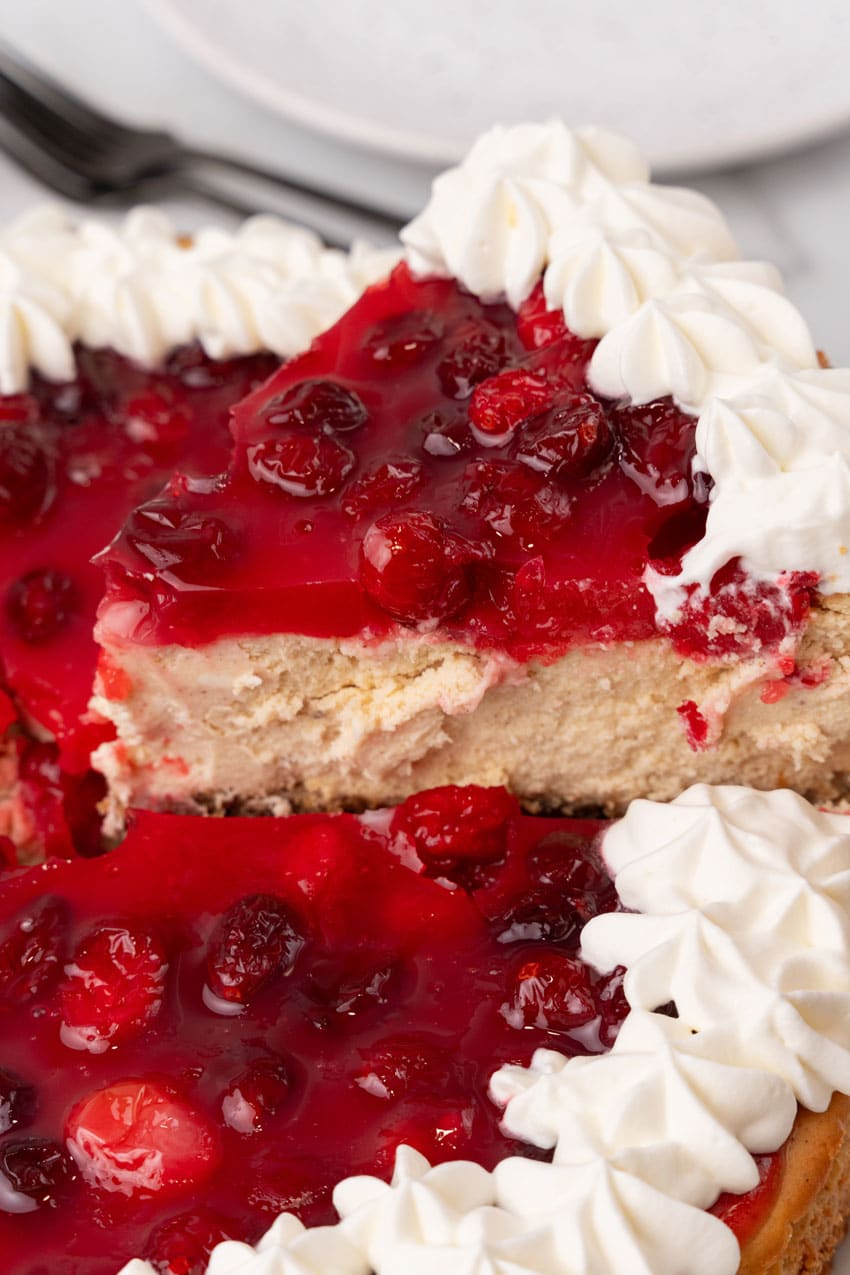 a cut slice of cranberry sauce topped cheesecake being lifted up by a spatula