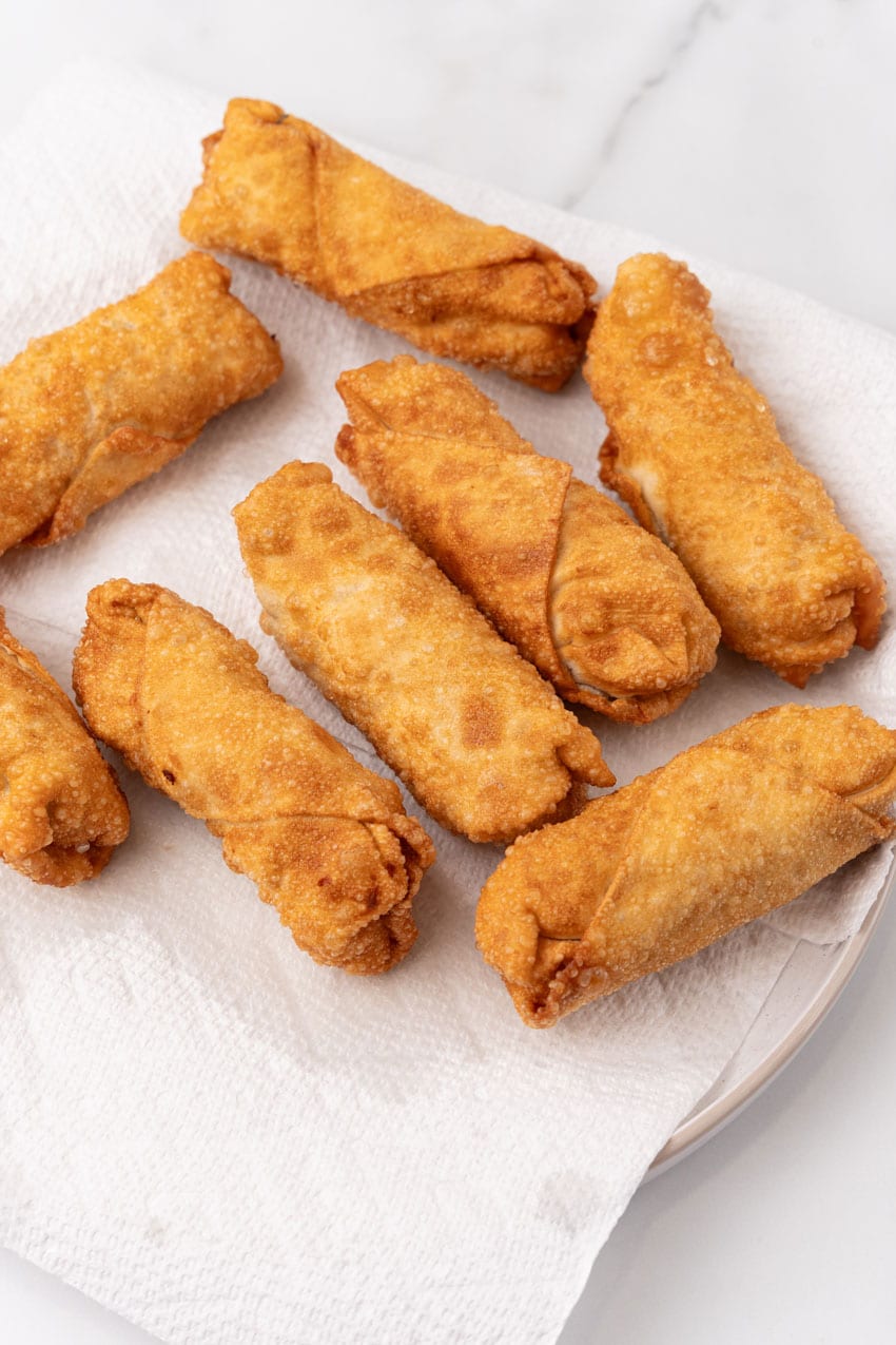 freshly fried egg rolls draining on a paper towel lined plate