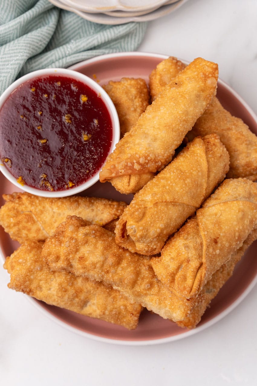 leftover thanksgiving egg rolls stacked on a dinner plate with a small white bowl of cranberry sauce on the side