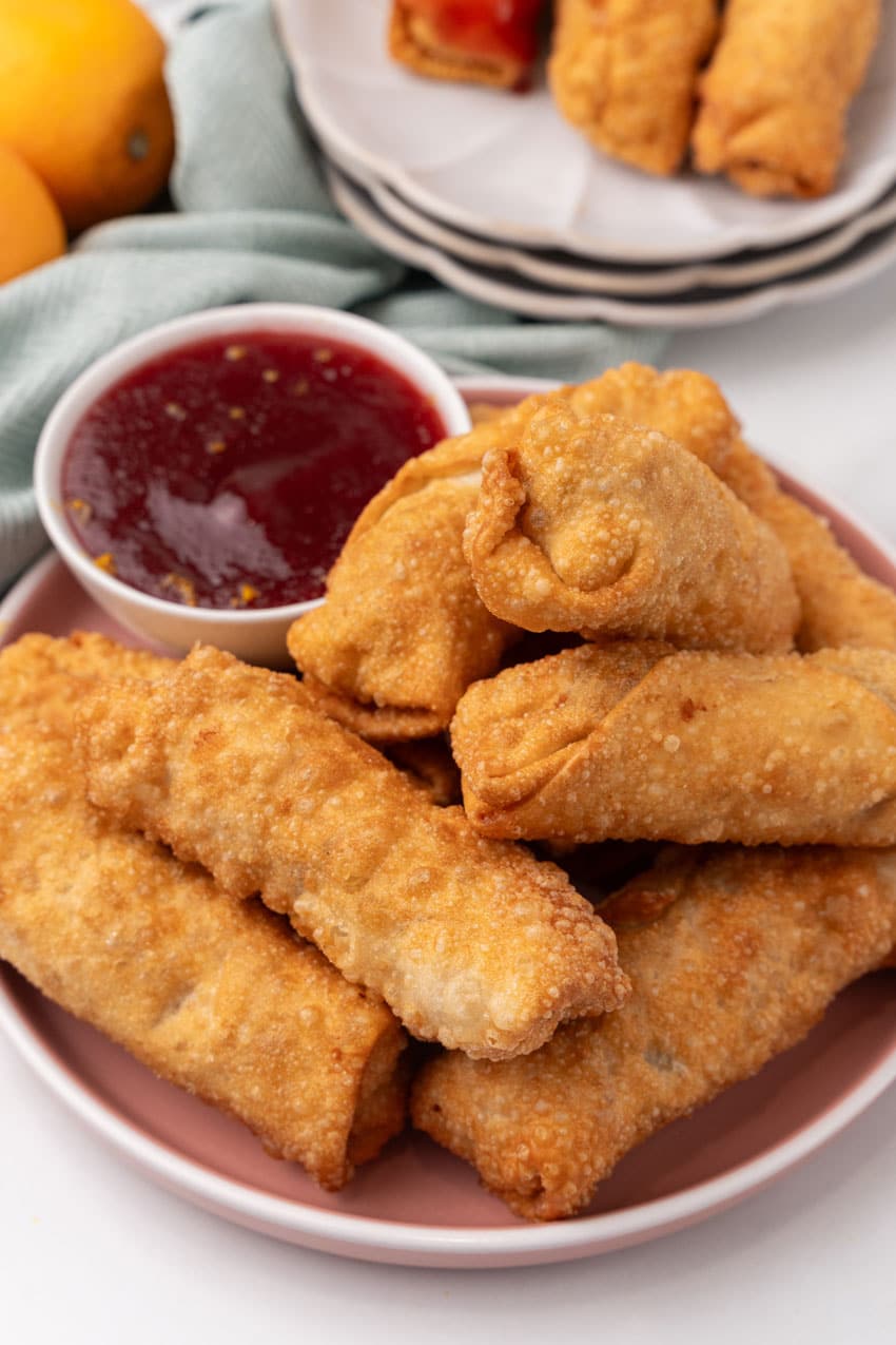 leftover thanksgiving egg rolls stacked on a dinner plate with a small white bowl of cranberry sauce on the side